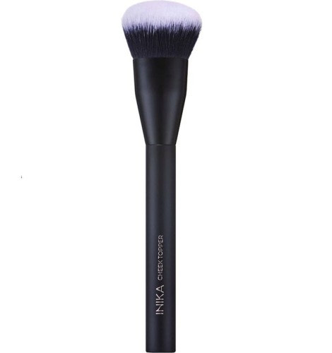 Na zdjęciu widoczny jest pędzel INIKA Organic Cheek Topper Brush. Ma gęste, miękkie, syntetyczne włosie o zaokrąglonym kształcie trzonek pędzla wykonany jest w eleganckim matowym, czarnym wykończeniu, z nazwą marki