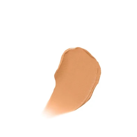 Na zdjęciu jest próbka korektora Jane Iredale Enlighten Concealer, w formie rozsmarowanej kremowej kropli. Próbka ma ciepły, beżowo-brzoskwiniowy odcień.