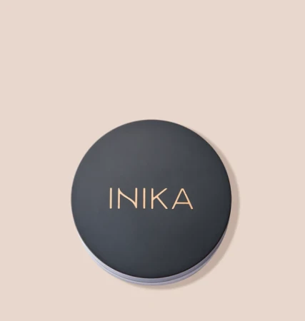 Na zdjęciu znajduje się okrągły pojemnik z czarną matową zakrętką. Na wieczku widoczny jest złoty napis „INIKA”. Produkt ustawiony jest na jasnym, beżowym tle. Całość prezentuje się minimalistycznie i elegancko