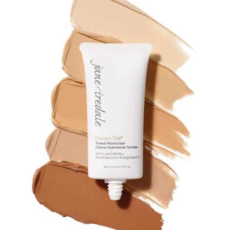 OpakowanieJANE IREDALE Dream Tint Tinted Moisturizer to elegancka tubka z miękkiego plastiku w kolorze beżowym, z delikatnymi złotymi akcentami. Ma praktyczny otwór dozujący, umożliwiający łatwą aplikację. Produkt na tle różnych odcieni.