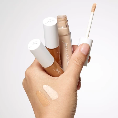 Na zdjęciu widać dłoń trzymającą trzy korektory PureMatch Liquid Concealer w różnych odcieniach. Jeden z korektorów ma odkręconą nakrętkę i aplikator z gąbeczką. Na wierzchu dłoni znajdują się próbki kolorów – jeden bardzo jasny, drugi bardziej beżowy.