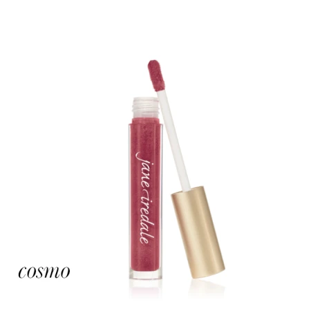 Na zdjęciu znajduje się błyszczyk do ust marki Jane Iredale w odcieniu Cosmo. Produkt zamknięty jest w eleganckim, przezroczystym opakowaniu z aplikatorem i złotą zakrętką. Kolor błyszczyka to głęboki róż z subtelnym, perłowym połyskiem