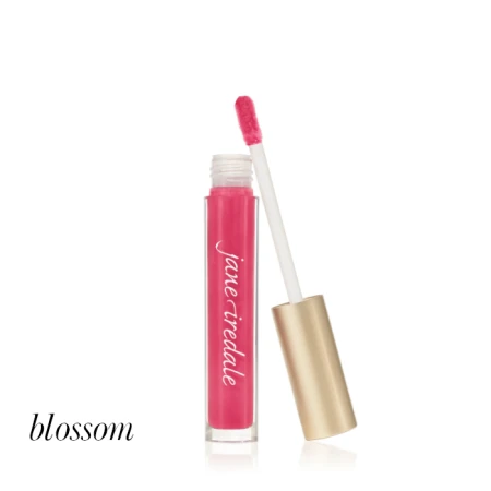 Na zdjęciu widoczny jest błyszczyk do ust marki Jane Iredale w odcieniu Blossom. Produkt znajduje się w przezroczystym opakowaniu z aplikatorem z miękką końcówką oraz elegancką, złotą nakrętką. Blossom to intensywny, świeży róż o soczystym wykończeniu