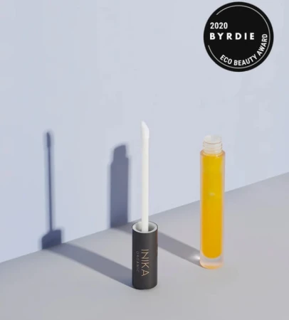 Na zdjęciu znajduje się elegancki kosmetyk marki INIKA ORGANIC–szklana buteleczka z żółtym płynem, obok stoi wyjęty aplikator z ciemną nakrętką i białym patyczkiem zakończonym gąbeczką. W górnym rogu jest odznaka „2020 BYRDIE ECO BEAUTY AWARD”