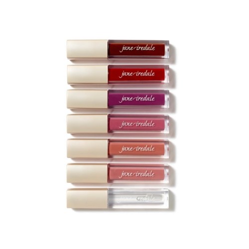 Na zdjęciu znajduje się zestaw błyszczyków marki Jane Iredale. Produkty ułożone są pionowo, jeden nad drugim, w eleganckich opakowaniach z beżową nakrętką i przezroczystym korpusem, przez który widać kolor błyszczyka.