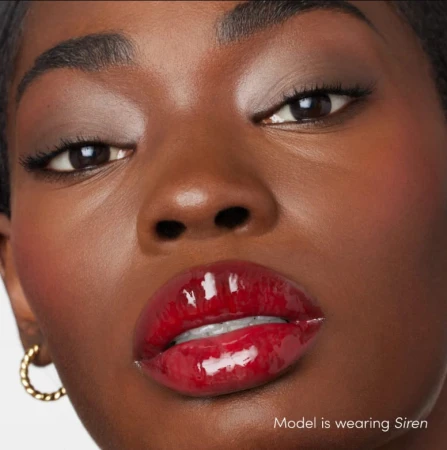 Na zdjęciu widzimy modelkę noszącą błyszczyk do ust Jane Iredale w odcieniu Siren. Usta modelki pokryte są intensywnie czerwonym błyszczykiem o wysokim połysku. Ten odcień świetnie podkreśla urodę i dodaje charakteru