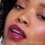 Na zdjęciu widzimy modelkę noszącą błyszczyk do ust Jane Iredale w odcieniu Juicy. Usta modelki pomalowane są błyszczykiem w intensywnym, soczystym odcieniu fioletowej śliwki.