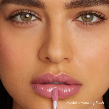 Na zdjęciu widzimy modelkę noszącą błyszczyk do ust Jane Iredale w odcieniu Flush. Flush to świeży, różany odcień z delikatnie chłodnym tonem. Usta modelki wyglądają pełniej i bardziej nawilżone dzięki połyskującej formule błyszczyka.