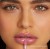 Na zdjęciu widzimy modelkę noszącą błyszczyk do ust Jane Iredale w odcieniu Flush. Flush to świeży, różany odcień z delikatnie chłodnym tonem. Usta modelki wyglądają pełniej i bardziej nawilżone dzięki połyskującej formule błyszczyka.