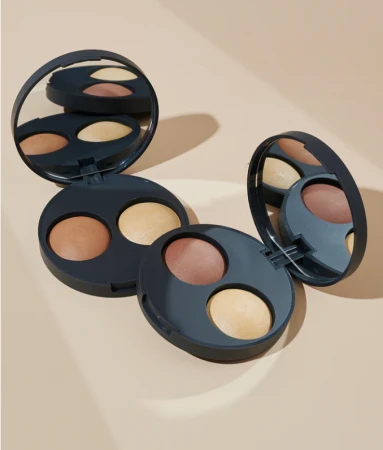 Na zdjęciu przedstawiono dwa otwarte kosmetyki marki INIKA Organic – Baked Contour Duo w dwóch różnych odcieniach. Każde opakowanie zawiera dwa wypiekane produkty w kamieniu: jeden w ciemniejszym odcieniu, a drugi w jaśniejszym (rozświetlacz).