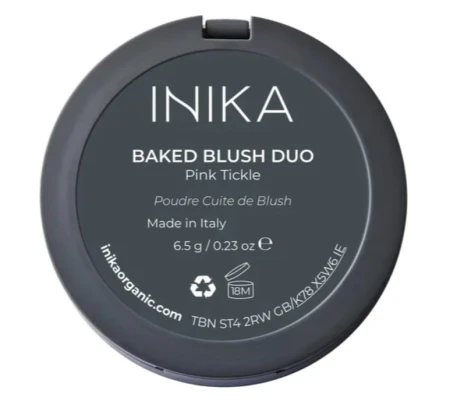 Na zdjęciu widoczny jest okrągły kosmetyk w czarnym opakowaniu z zamknięciem na zatrzask. Na pokrywce znajduje się biały napis „INIKA BAKED BLUSH DUO Pink Tickle”. Pod nim umieszczone są dodatkowe informacje