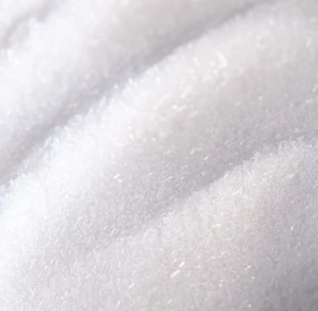 Zbliżenie na białe, drobnoziarniste kryształki soli kosmetycznej lub peelingu w proszku o delikatnej, puszystej teksturze – produkt używany w pielęgnacji stóp lub ciała.