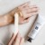 Na zdjęciu pokazano aplikację peelingu Elim MEDIHAND Hydro-Thermal Peel na dłoń. Produkt jest nakładany za pomocą szpatułki, co podkreśla jego profesjonalne i pielęgnacyjne zastosowanie do złuszczania i wygładzenia skóry rąk.
