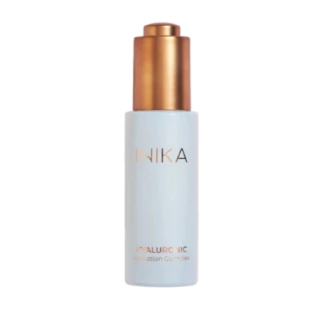 Na zdjęciu znajduje się kosmetyk marki INIKA Organic – Hyaluronic Hydration Complex.  To elegancka, smukła buteleczka w jasnoniebieskim kolorze z metaliczną złotą pompką i subtelnym napisem „INIKA” w odcieniu różowego złota.