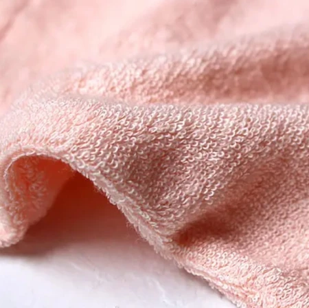 Na zdjęciu jest rękawica Magic Mitt marki Jane Iredale – wykonana z miękkiego, delikatnego materiału o jasnoróżowym kolorze. Posiada metkę z nazwą marki.