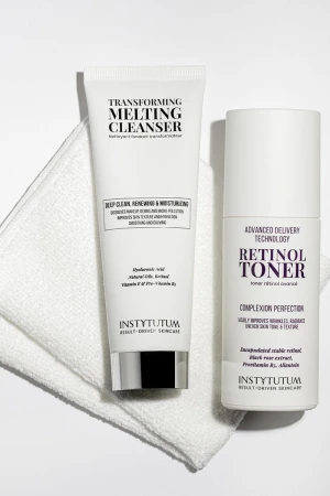 Na białym ręczniku stoją dwa produkty Instytutum: Transforming Melting Cleanser w tubce (oczyszczająco-nawilżający żel) i Retinol Toner w butelce z pompką (tonik wygładzający z retinolem). Opakowania białe z czarnym i fioletowym tekstem.