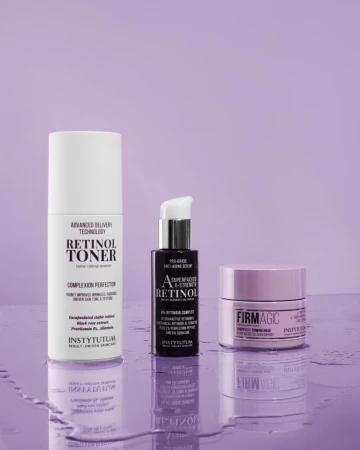 Trzy produkty Instytutum na fioletowym tle: Retinol Toner w białej butelce, serum w ciemnofioletowym opakowaniu z pompką i krem Firm Magic w fioletowym słoiczku. Powierzchnia z lekkim odbiciem i kroplami wody.