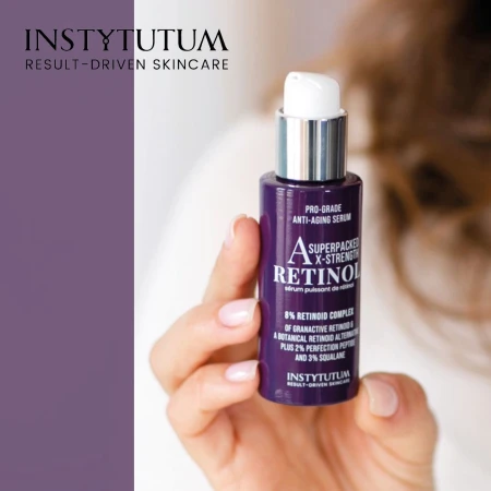 Dłoń trzyma fioletową butelkę serum Instytutum Superpacked X-Strength Retinol z białą pompką i srebrną nakrętką. W tle logo Instytutum na fioletowym pasku. Serum zawiera 8% retinoid complex, peptydy i skwalan, działa przeciwstarzeniowo.