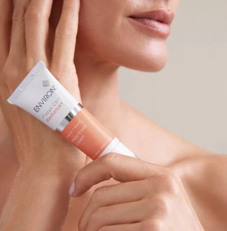 Zbliżenie na damskie dłonie, trzymające tubkę kremu ENVIRON C-Boost Mela-Even Cream.