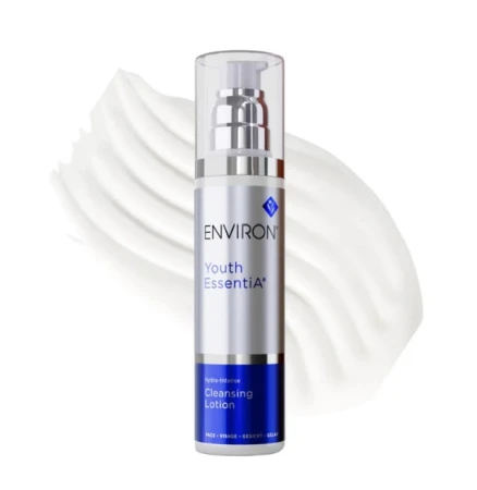 Butelka mleczka ENVIRON Cleansing Lotion w kolorze srebrnym, ze srebrną nakrętką i granatową etykietą, na tle próbki tego produktu w formie białej, rozsmarowanej kropli kremu.