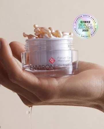 Kobieca dłoń trzyma otwarty słoik z kapsułkami, kilka z nich jest otwartych i oleisty płyn ścieka po palcach. U góry logo zdobytej nagrody Glamour Beauty Award 2023.