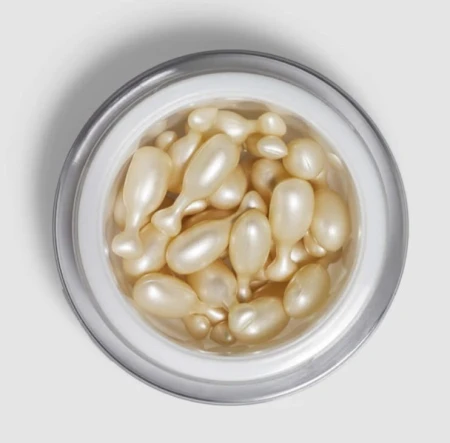 Widok od góry, na otwarty słoiczek ENVIRON Hydrating Oil Capsules, gdzie są umieszczone kapsułki w kształcie rybki i w kolorze perłowym.