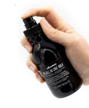 Ręka trzymająca butelkę Davines OI All In One Milk o pojemności 135 ml. Czarne opakowanie z atomizerem i białym napisem wskazującym na wielofunkcyjny kosmetyk pielęgnacyjny do włosów.