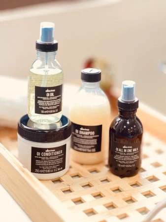 Zestaw czterech produktów do pielęgnacji włosów Davines z linii OI ustawiony w bambusowej tacy: OI Oil, OI Shampoo, OI Conditioner i OI All in One Milk. Każdy produkt ma charakterystyczną czarną etykietę i estetyczne, minimalistyczne opakowanie.