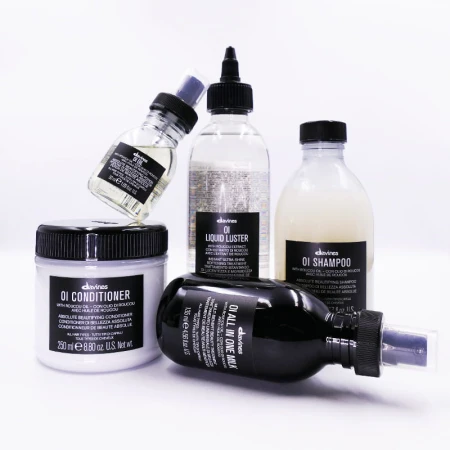 Pięć produktów do pielęgnacji włosów marki Davines z serii OI: szampon, odżywka, liquid luster, all in one milk i olejek; ustawione na jasnym tle, wszystkie z charakterystycznymi czarnymi etykietami.