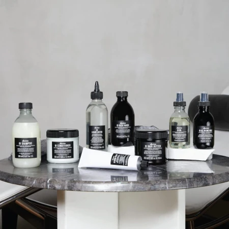 Zestaw produktów do pielęgnacji włosów marki Davines z linii OI ustawiony na marmurowym stoliku; wśród nich szampon, odżywka, olejek, mleczko, masełko i lotion, wszystkie w charakterystycznych czarno-białych opakowaniach.