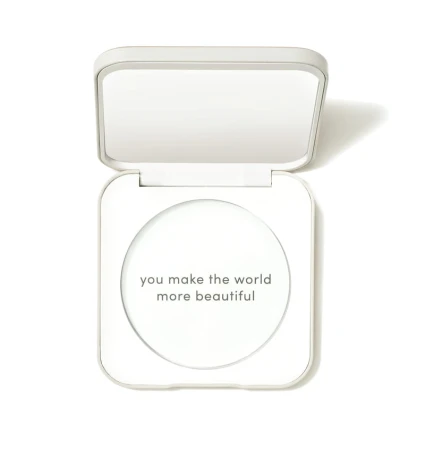 Na zdjęciu jest kompaktowe opakowanie wielokrotnego użytku marki jane iredale. Minimalistyczny, elegancki design w kolorze białym, napis na froncie: “you make the world more beautiful. Widać lusterko pod wieczkiem.