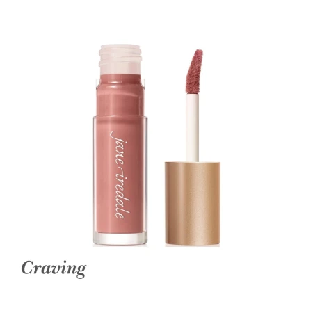 Na zdjęciu przedstawiony jest błyszczyk do ust Jane Iredale w odcieniu Craving. Produkt zamknięty jest w eleganckim opakowaniu z przezroczystą tubką i złotą nakrętką. Odcień Craving to jasny, stonowany róż z nutą łososia