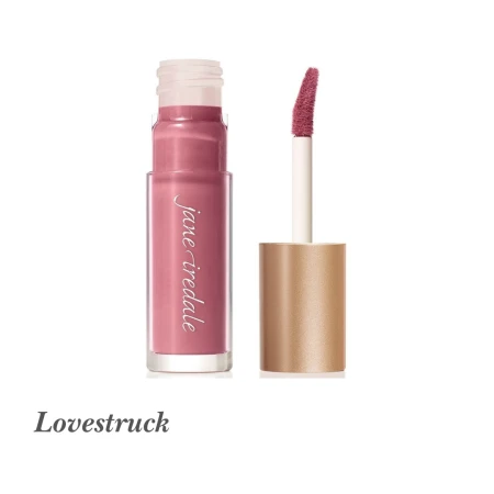 Na zdjęciu przedstawiony jest błyszczyk do ust Jane Iredale w odcieniu Lovestruck. Produkt ma eleganckie, przezroczyste opakowanie z nazwą marki oraz złotą nakrętką, pod którą znajduje się wygodny aplikator z gąbeczką. Lovestruck to chłodny, średni róż