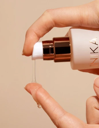 Zdjęcie przedstawia aplikację INIKA Adaptogenic Cleansing Oil – olejku oczyszczającego o lekkiej, oleistej konsystencji. Widzimy przezroczysty olejek spływający na palce, co podkreśla jego delikatną formułę