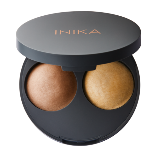 Na zdjęciu znajduje się otwarte opakowanie INIKA Organic Baked Highlight Duo – wypiekany rozświetlacz w dwóch odcieniach. Produkt umieszczony jest w eleganckim, czarnym kompaktowym etui z logo INIKA w kolorze miedzianym na wieczku.