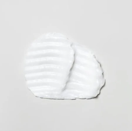 Biała, gęsta konsystencja produktu do pielęgnacji włosów (Davines OI Hair Butter) na jasnym tle, uformowana w owalny kształt z wyraźnymi żłobieniami w strukturze.