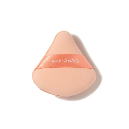 Na zdjęciu jest gąbka do makijażu marki jane iredale,  służąca do nakładania podkładu. Beżowy materiał,  trójkątny kształt – idealny do precyzyjnej aplikacji w okolicach oczu i nosa.
