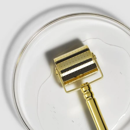 W płytkim naczyniu napełnionym płynem Cleaning Solution leży głowica złotego rollera (Gold-Cita).