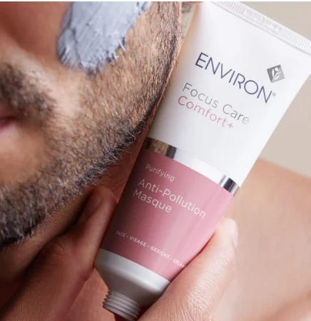 Zbliżenie na tubkę maski Environ Focus Care Comfort+ Anti-Pollution Masque dotykającej męskiej skóry twarzy na której jest próbka maski w kolorze szarym.