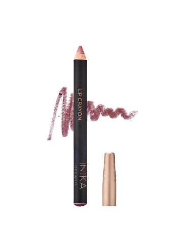 Na zdjęciu widoczna jest kredka do ust (Lip Crayon) marki INIKA Organic. Produkt ma elegancki czarny korpus z napisami w odcieniu złota. Obok znajduje się złocona skuwka. W tle widać próbkę koloru w formie miękkiej kreski w odcieniu przygaszonego różu