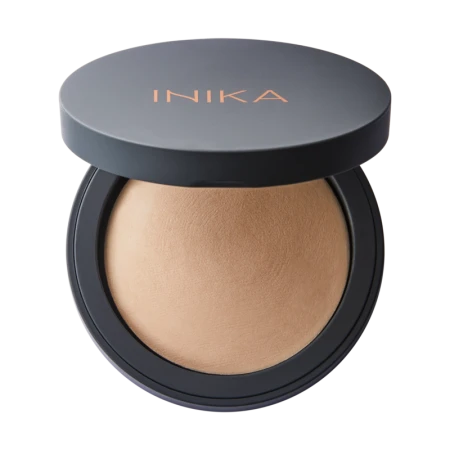Na zdjęciu widoczny jest otwarty kompaktowy puder marki INIKA Organic. Produkt znajduje się w eleganckim, czarnym opakowaniu z logo INIKA na pokrywce w kolorze miedzianym. Puder ma jednolitą, wypiekaną powierzchnię w odcieniu beżowym