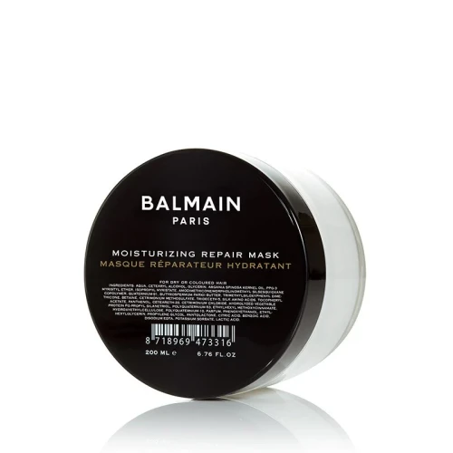 Na zdjęciu widoczna jest nawilżająca maska regenerująca do włosów Balmain Paris – Moisturizing Repair Mask. Produkt znajduje się w eleganckim, przezroczysto-białym słoiczku z czarnym, błyszczącym wieczkiem.