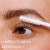 Na obrazie widzimy aplikację odżywki PureLash® Lash Extender & Conditioner od jane iredale na rzęsy. Produkt ma białą, kremową konsystencję, którą rozprowadza się szczoteczką o gęstym, spiralnym włosiu.