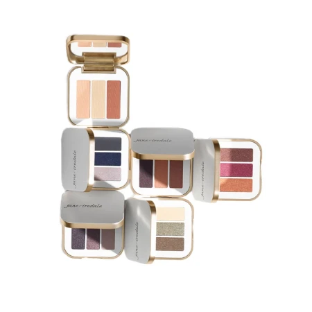 Zestaw sześciu potrójnych paletek cieni do powiek Jane Iredale PurePressed Eye Shadow Triple. Każda zawiera trzy odcienie, zamknięte w eleganckim białym kompakcie z lusterkiem i złotą ramką.  Paletki są pokazane w różnych układach, z różną kolorystyką.