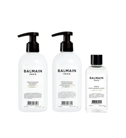 Zestaw kosmetyków Balmain Paris: dwa produkty w butelkach z pompką (szampon i odżywka), eliksir arganowy w mniejszej butelce oraz eleganckie pudełko prezentowe w bieli i złocie z spinką do włosów wewnątrz