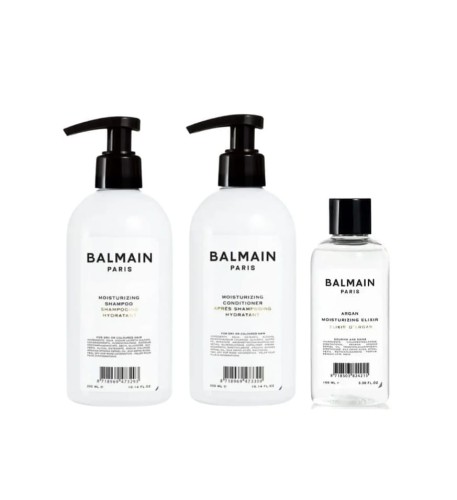 Zestaw kosmetyków Balmain Paris: dwa produkty w butelkach z pompką (szampon i odżywka), eliksir arganowy w mniejszej butelce oraz eleganckie pudełko prezentowe w bieli i złocie z spinką do włosów wewnątrz