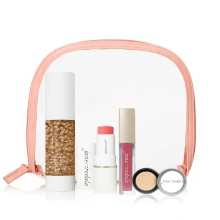 Elegancki zestaw jane iredale zapakowany w przezroczystą kosmetyczkę z różową ramką. W środku jest: podkład w płynie z kapsułkami, sztyft różu, błyszczyk do ust, korektor w słoiczku oraz pomadka. Całość prezentuje się świeżo i luksusowo.
