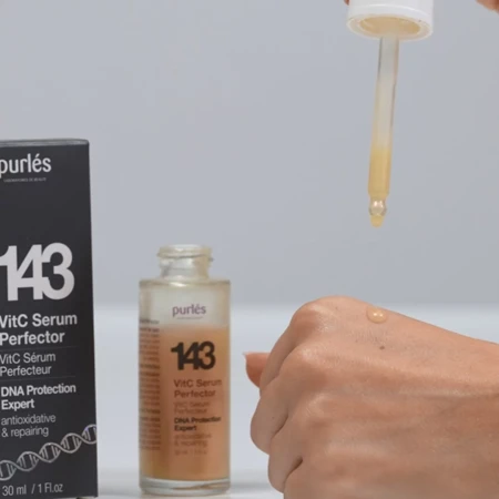 Kobieca dłoń, na którą z pipety spada kropla serum o lekko pomarańczowym odcieniu. Ujęcie pokazuje konsystencję produktu i sposób aplikacji, podkreślając jego pielęgnacyjny charakter.