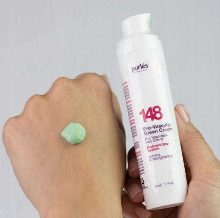 W prawej dłoni trzymana jest biała butelka Purles 148 Pro-Vascular Green Cream. Na lewej dłoni  jest próbka kremu w kolorze zielonym. To prezentacja  konsystencji jak i odcienia, co daje wyobrażenie o formule i zastosowaniu.