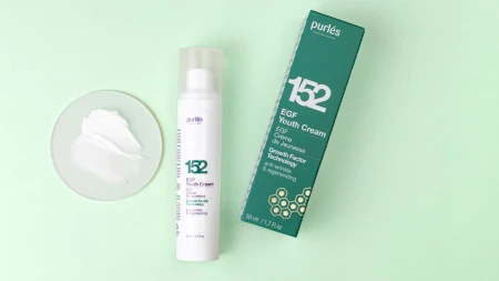 Na zdjęciu jest krem marki Purles EGF Youth Cream 152 w białym, smukłym opakowaniu z pompką oraz jego zielone pudełko. Obok, na szklanej płytce, jest próbka kremu w formie białej, gładkiej emulsji. Całość została sfotografowana na jasnym, miętowym tle.